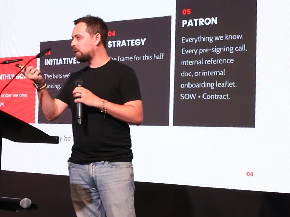Nicholas F. Hernandez on stage, speaking into a microphone and gesturing toward a slide of numbered planning cards